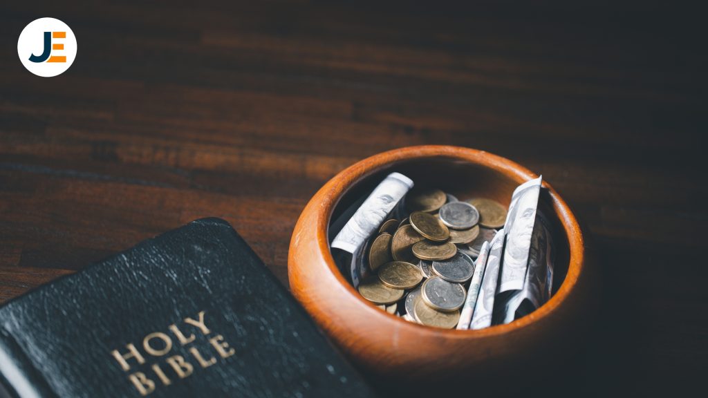 A wooden bowl with money in it sitting next to a bible on a wooden table